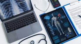 laptop with a chest-ray next to an digital tablet with a body scan image and a pad with handwritten medical notes, plus a stethoscope on the desk.